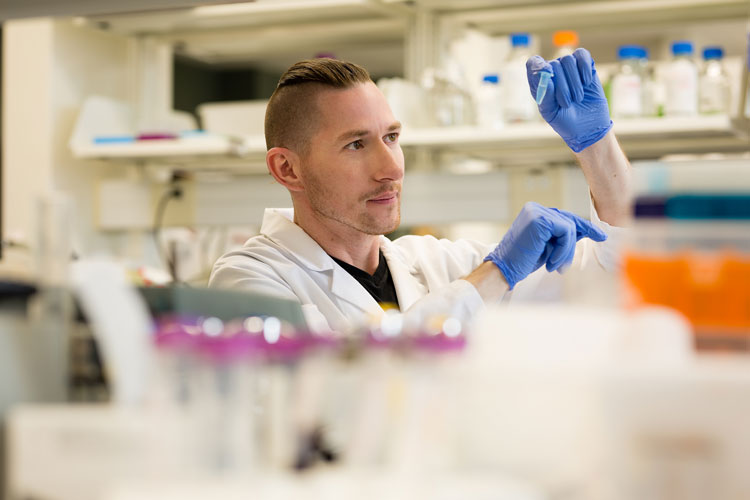 Dean Reddick examines a vial a lab, © Cory Aronec Photography