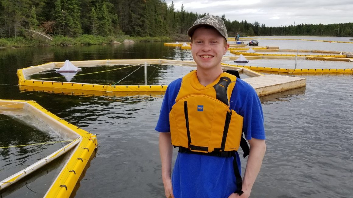 Daniel Denton standing in front of a lake wearing a yellow life jacket.