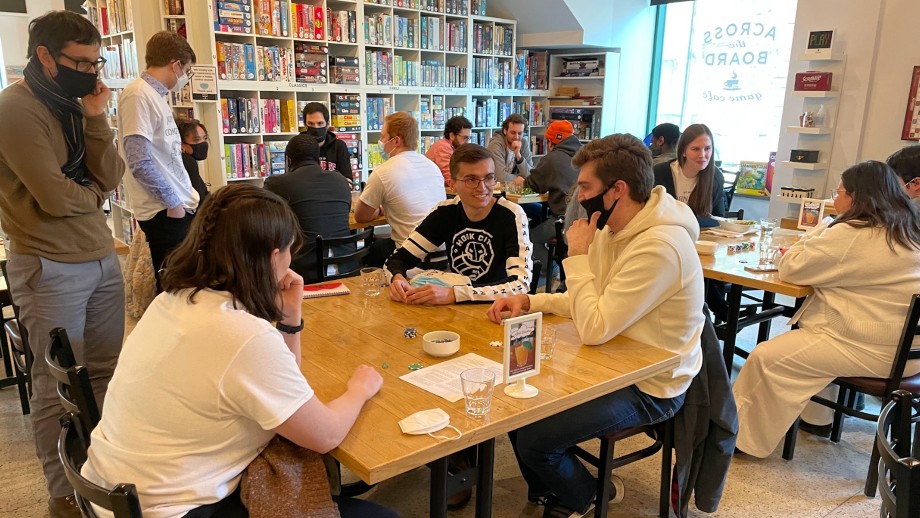 Groups of students playing board game around tables.