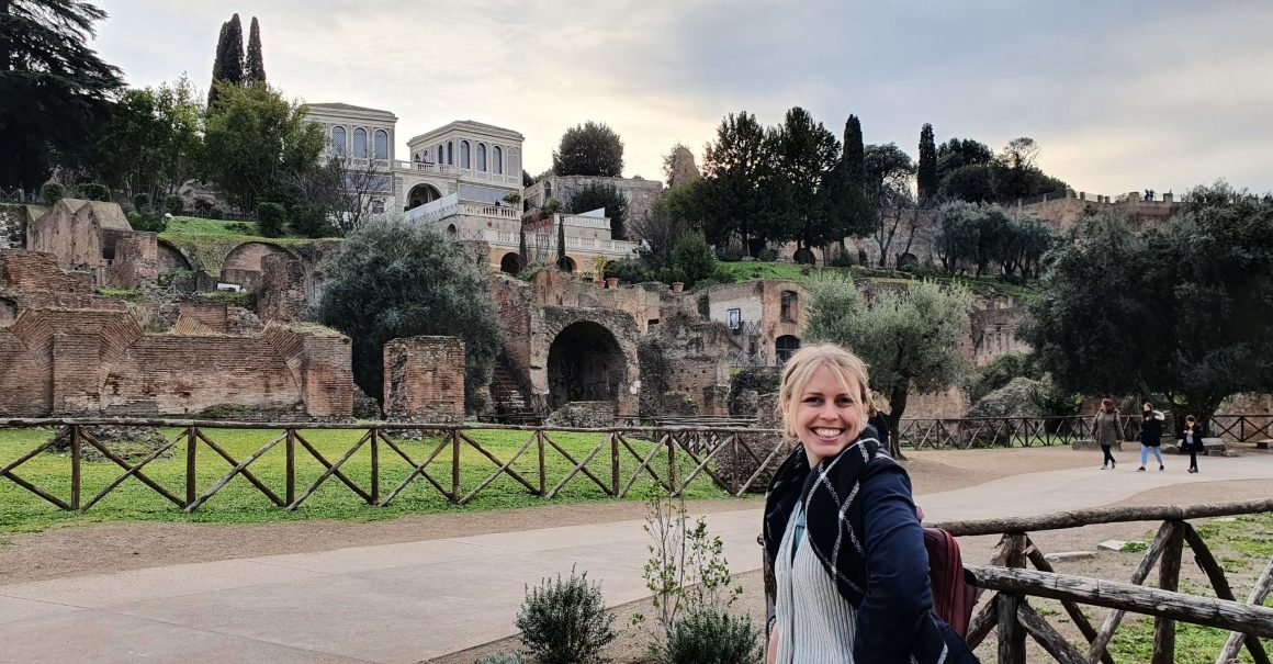 Ella Greer is standing in front of Roman ruins in Rome