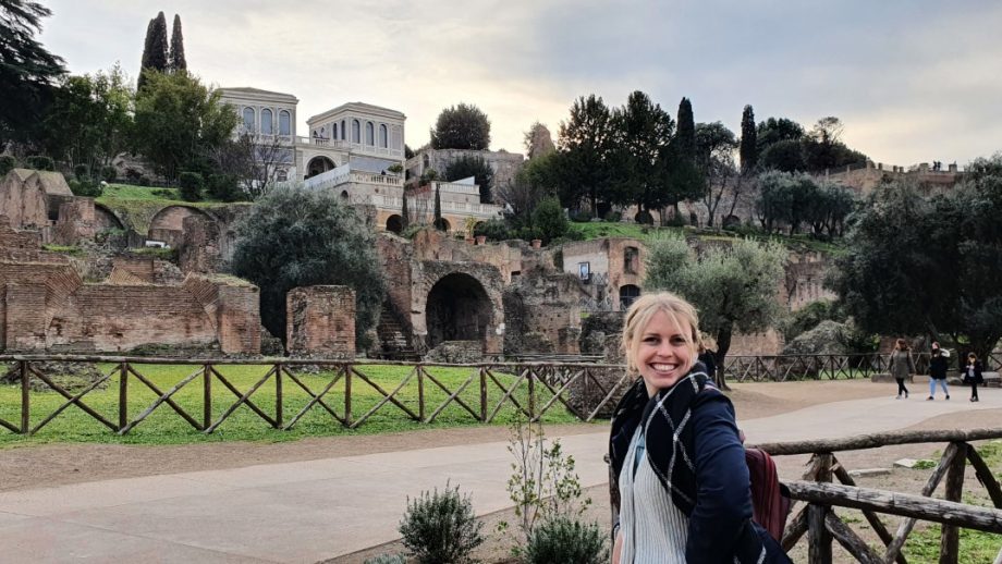 Ella Greer is standing in front of Roman ruins in Rome