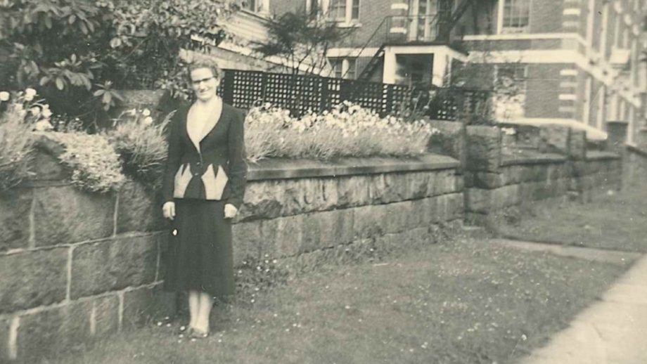Black and white photo of udy McConill standing in front of garden after her arrival to Canada.