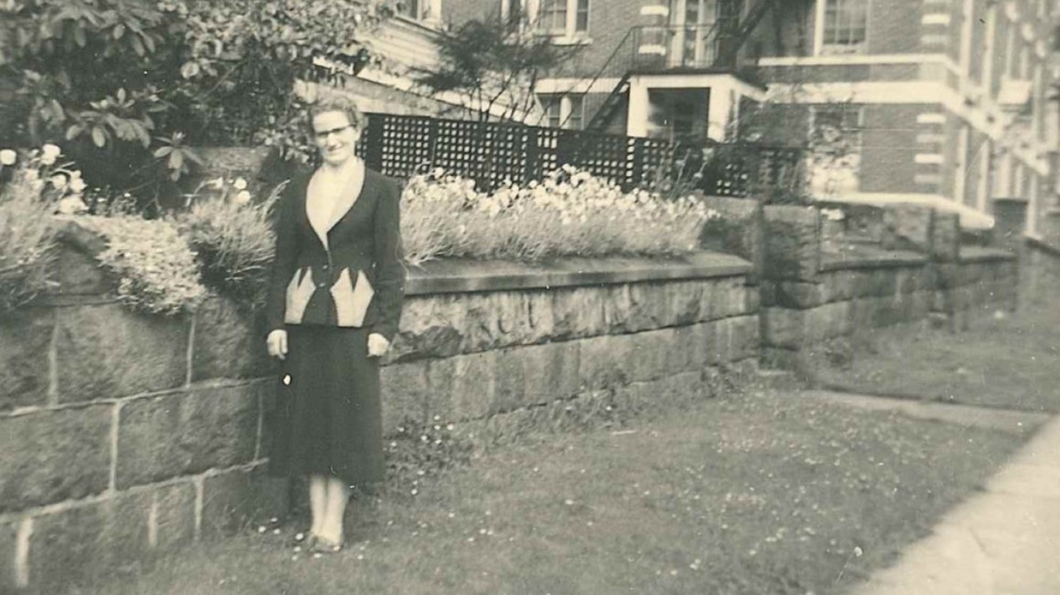 Black and white photo of udy McConill standing in front of garden after her arrival to Canada.