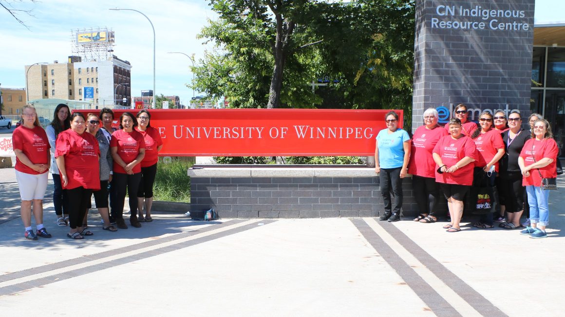 A group of Indigenous students standing out side by a UWinnipeg sign.