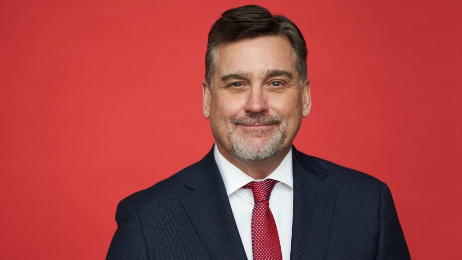 Head shot of Todd Mondor in front of a red background.