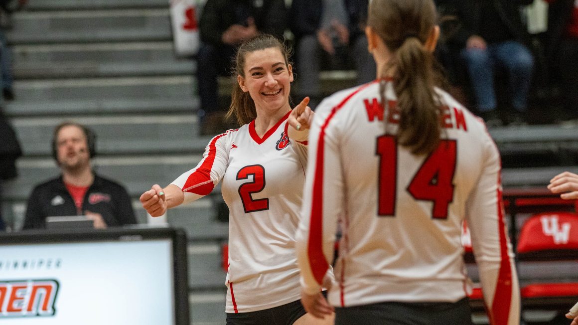 A volleyball player points at another while smiling in celebration