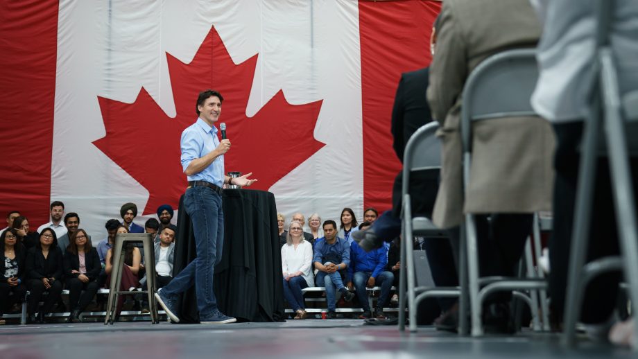 Prime Minister Justin Trudeau in front of a Canadian flag answering questions asked by audience members.