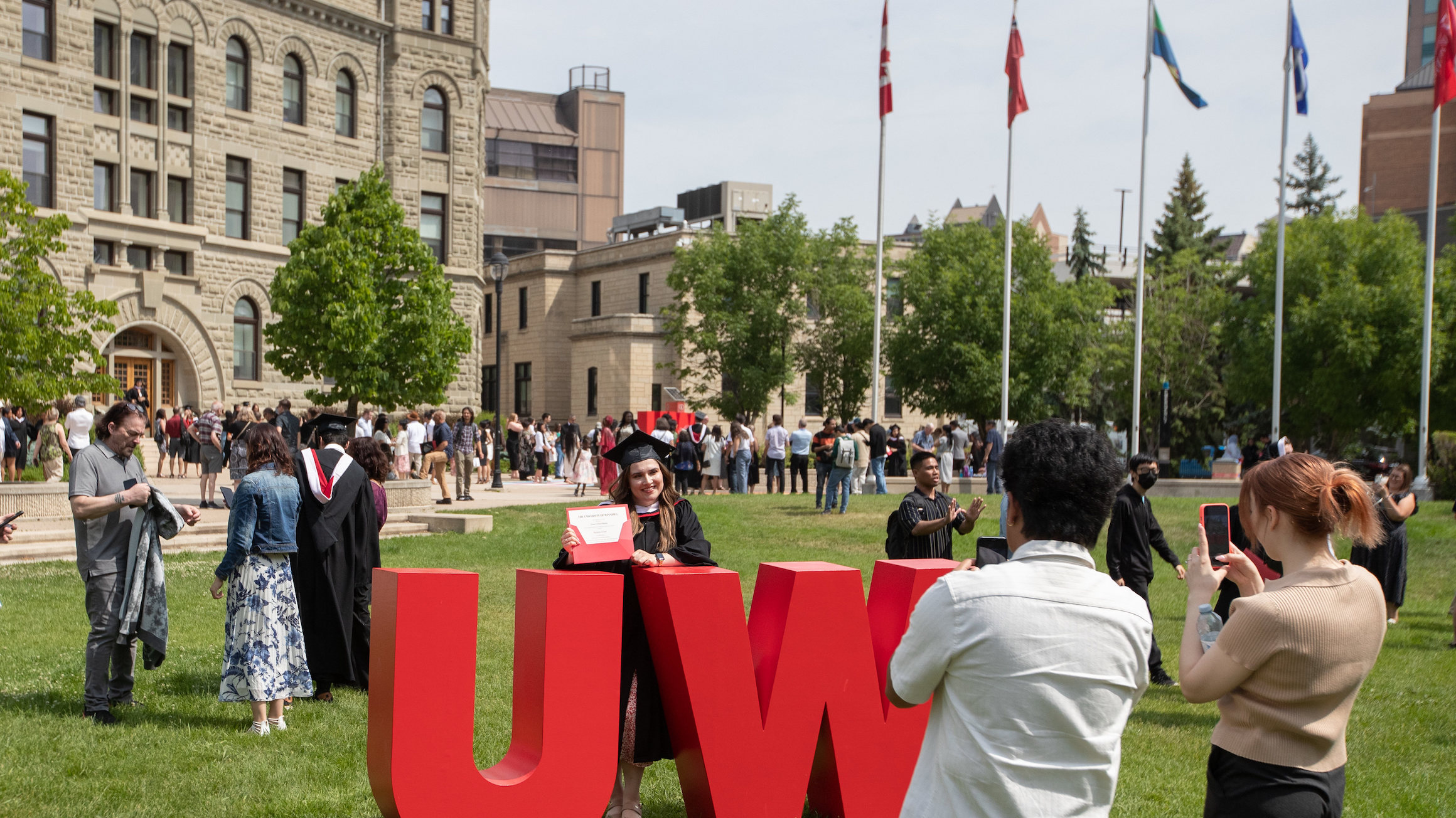 A graduate stands in front of the UW sign with Wesley Hall in the background.