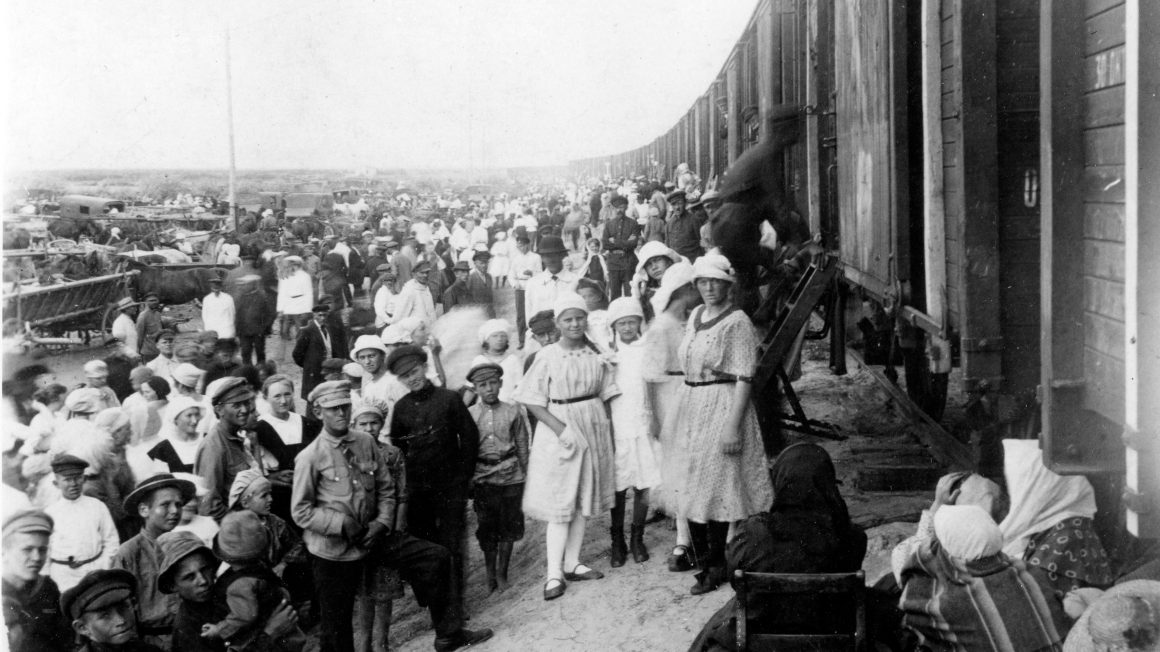 A black and white historical photograph depicts Mennonites boarding a train in the Soviet Union.