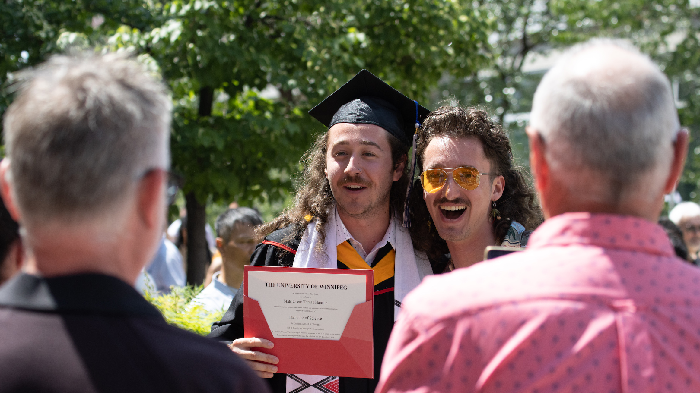 A graduate poses for a photo with a friend on campus.