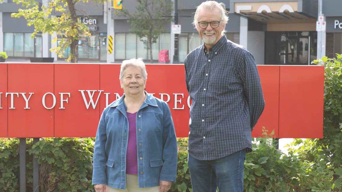 Theckla Brown and Roger Groening standing in front of the UWinnipeg sign.