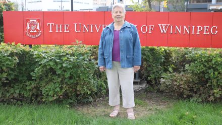 Theckla Brown in front of the UWinnipeg sign.