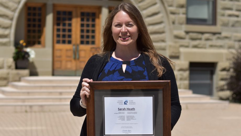 Sarah Heath in front of Wesley Hall holding a framed award certificate.