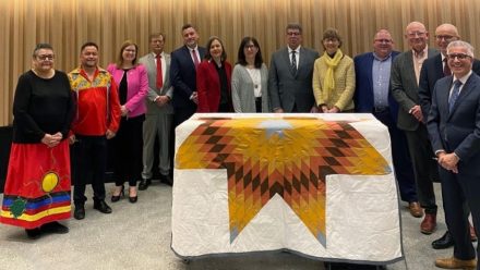 A group of people stand behind a table draped with a white and gold star quilt.
