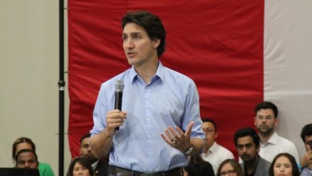 Justin Trudeau talks to a crowd with people seated behind him.