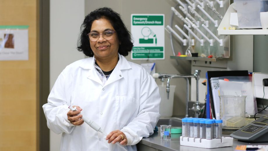 Dr. Srimathie Indraratne in her lab leaning on a silver table next to test tubes.