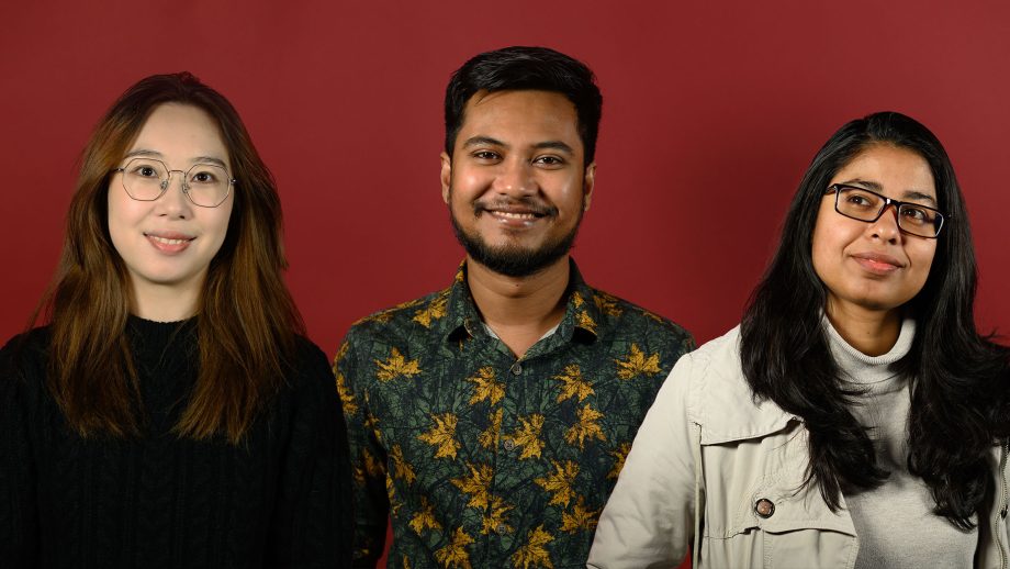 Three students stand in front of a red backdrop.