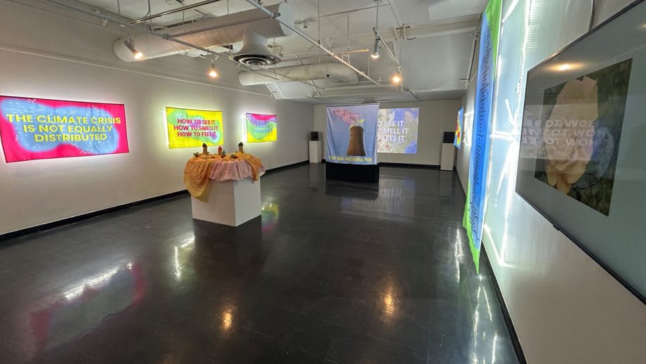 contemporary art installation in gallery features backlit banners, video, and podium with candles.