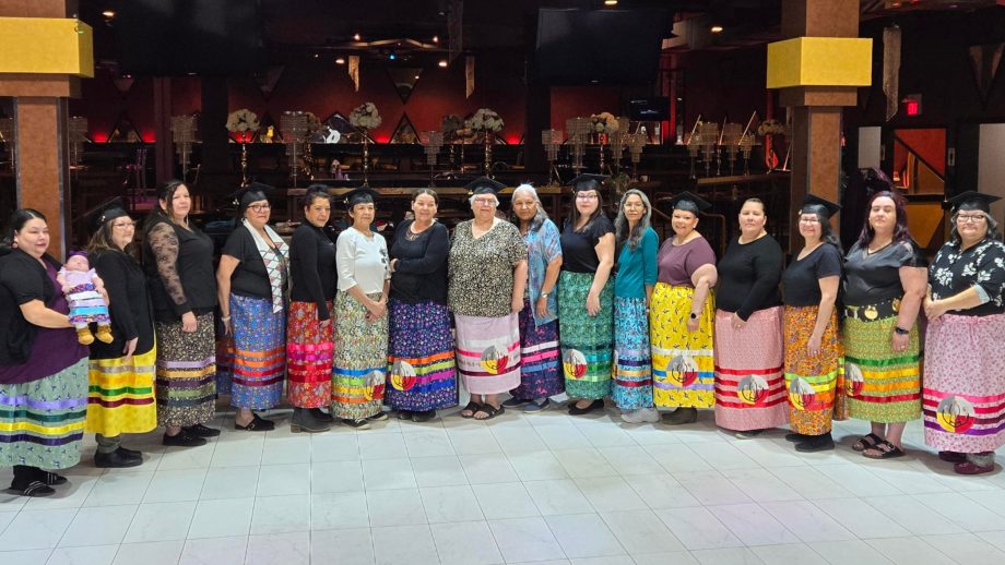 A group of women wearing ribbon skirts, standing in a semi circle.