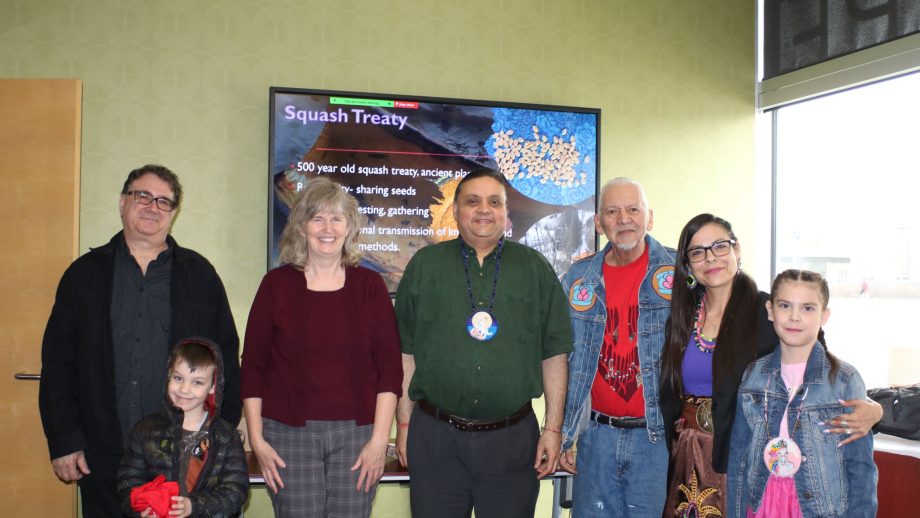 Dr. Mark Ruml, Dr. Shirley Thompson, Dr. Shailesh Shukla, Knowldege Keeper Dave Daniels, Anna Neil, and two children stand in a classroom with a video screen behind them.