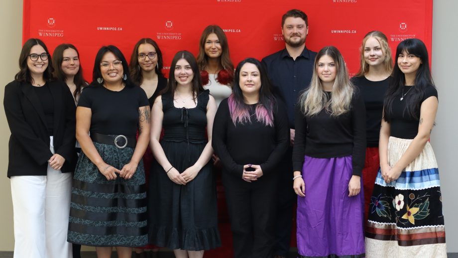 Eleven students stand in front of a red backdrop.