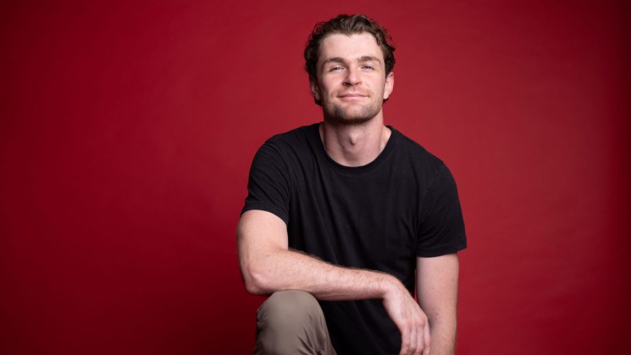 Donald Stewart with his arm resting on his knee in front of a red background.