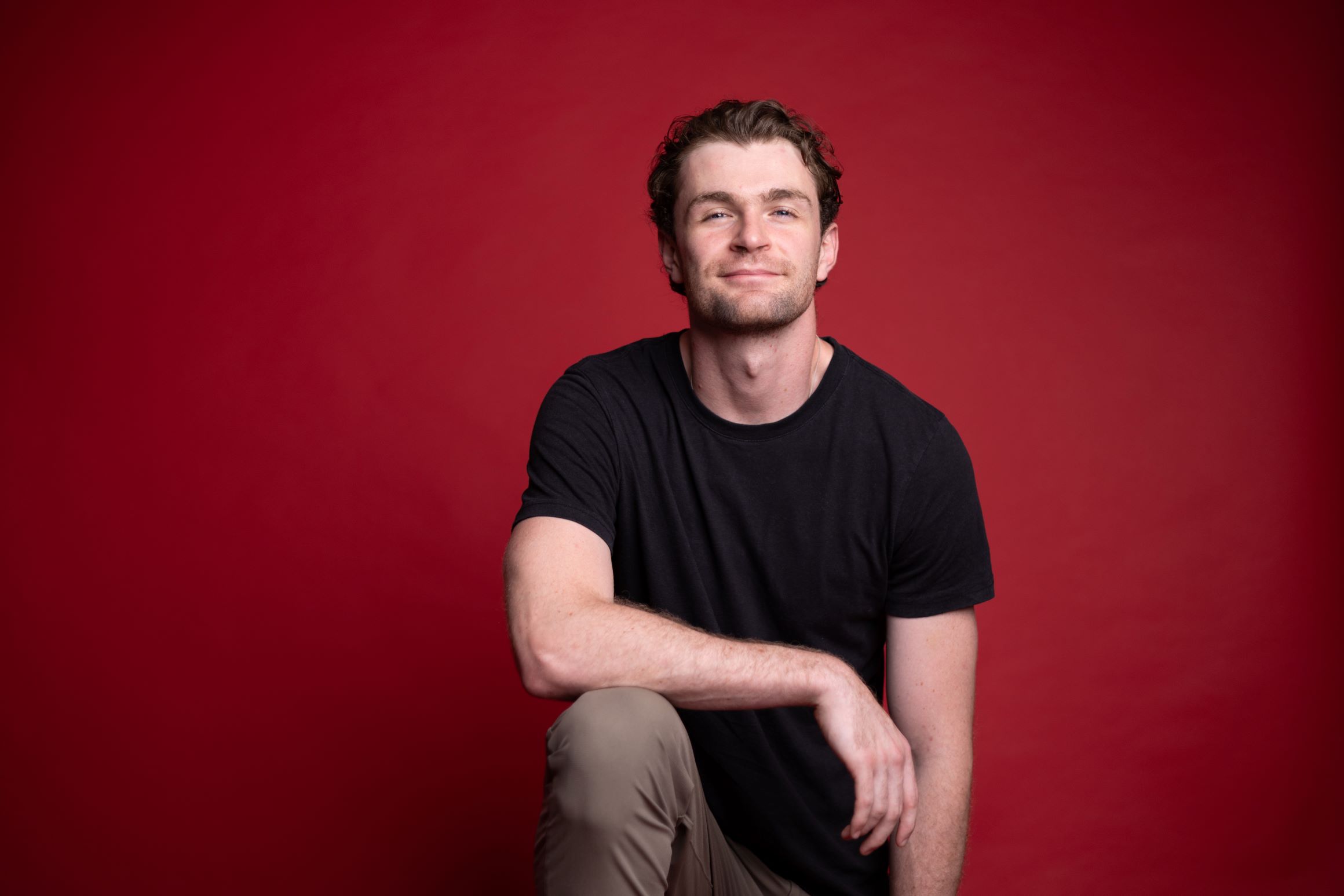 Donald Stewart with his arm resting on his knee in front of a red background.