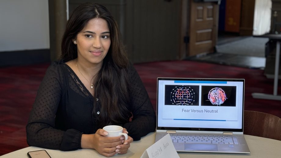 Student sits next to a laptop that displays a presentation page.