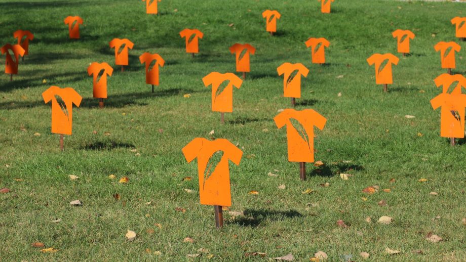 Several cutouts of orange t-shorts are installed on a lawn.