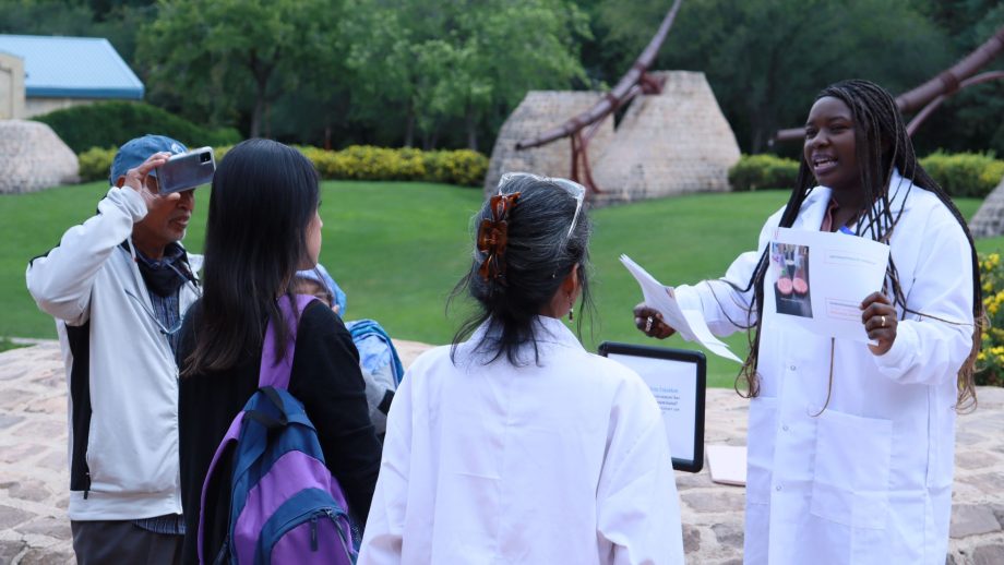 A scientist delivers an outdoor presentation to a group of onlookers.