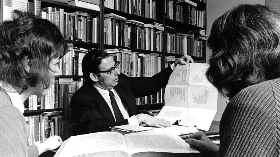 Professor and students sitting at a table in a library.