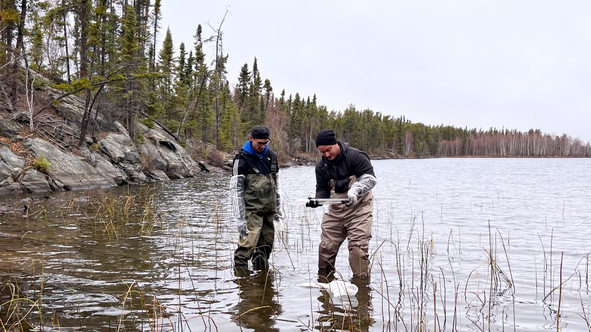 Two UWinnipeg students standing in the water on the edge of a lake.