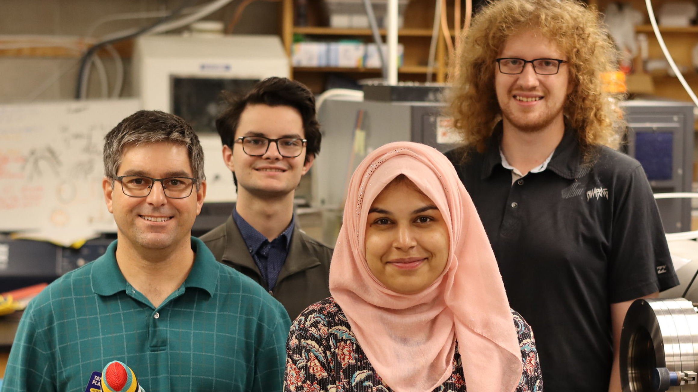 Dr. Russell Mammei, Thomas Hepworth, Abeer Zahra, Rylen De Vries standing in a physics lab