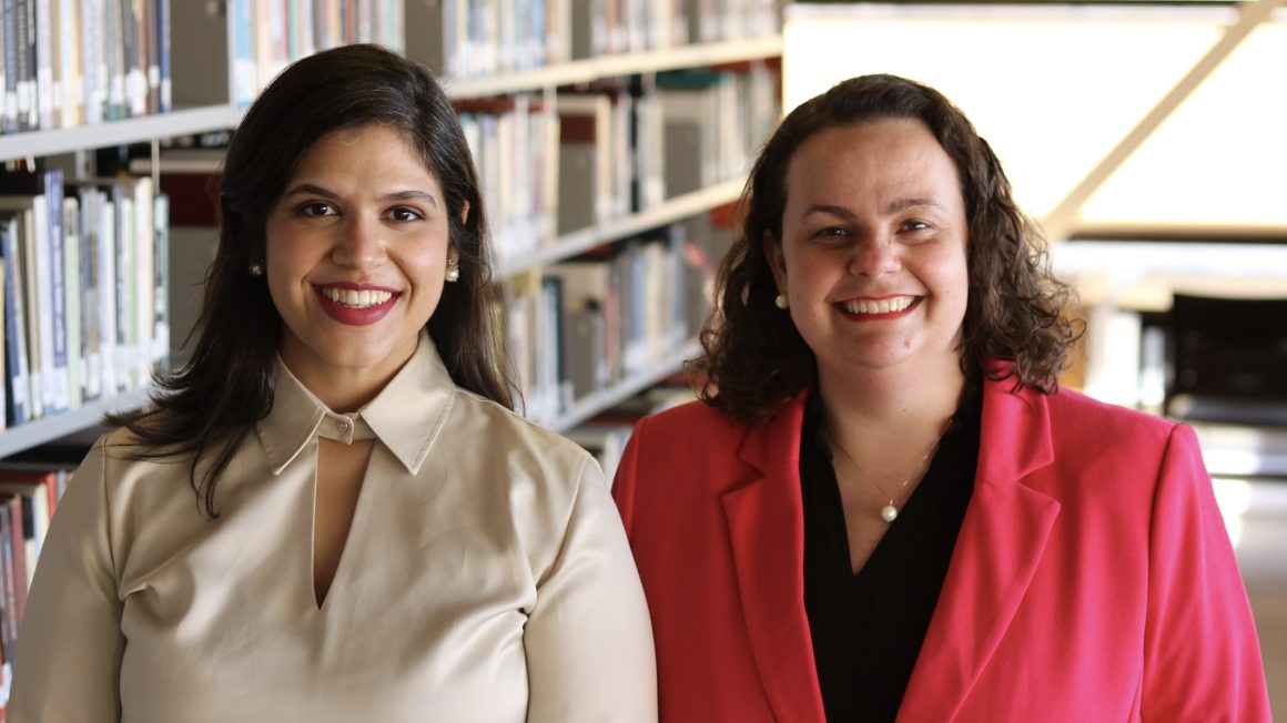 Maria Claudia Gastal Ramos and Dr. Flavia Amaral standing in front of book shelves in the library