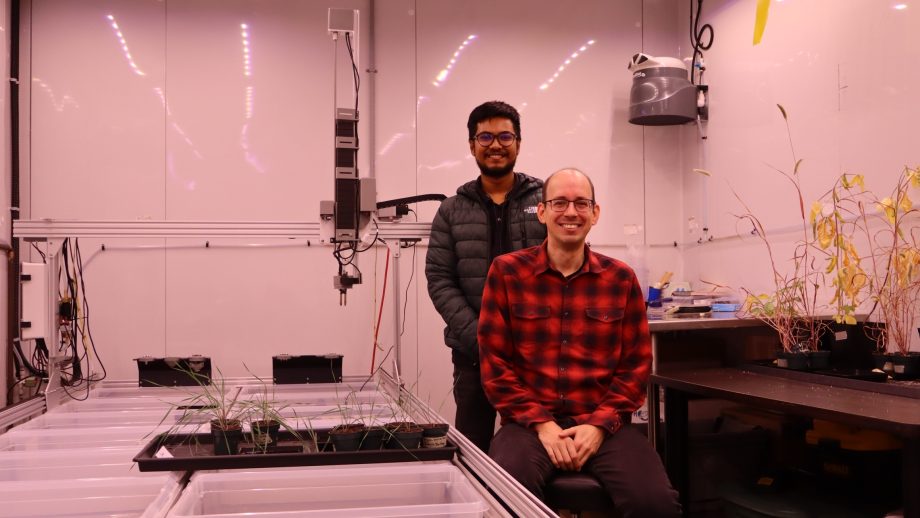 Two men display plant seedlings in a walk-in growing chamber.