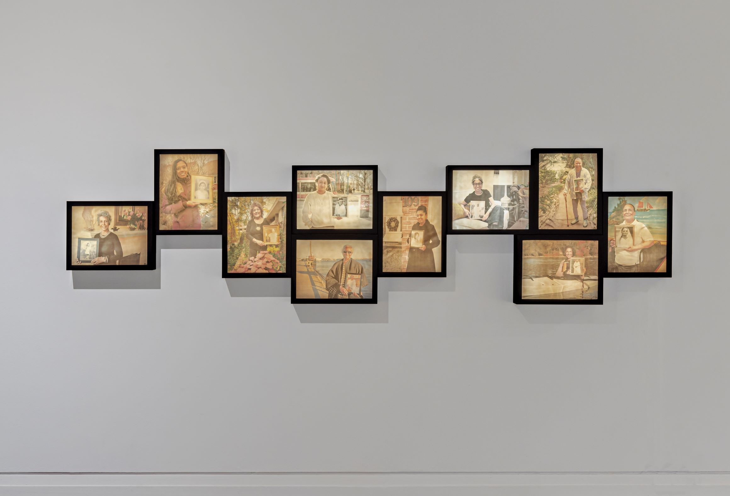 Portraits in a staggered formation on a grey wall.