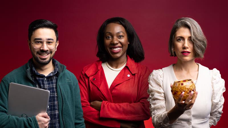 Three students, one holding a laptop, one with folded arms, and one holding a ceramic object, stand in front of a red background.