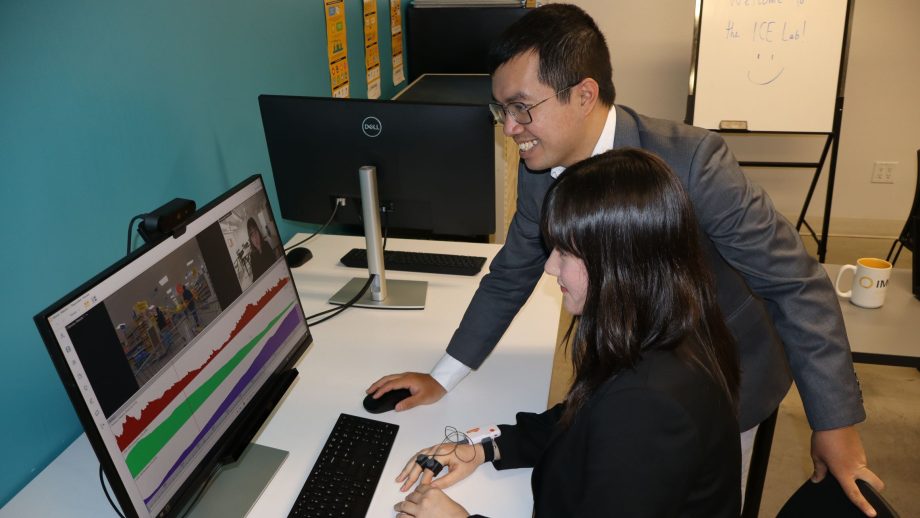 In a classroom, a male professor and a female student use a desktop computer equipped with special marketing software.