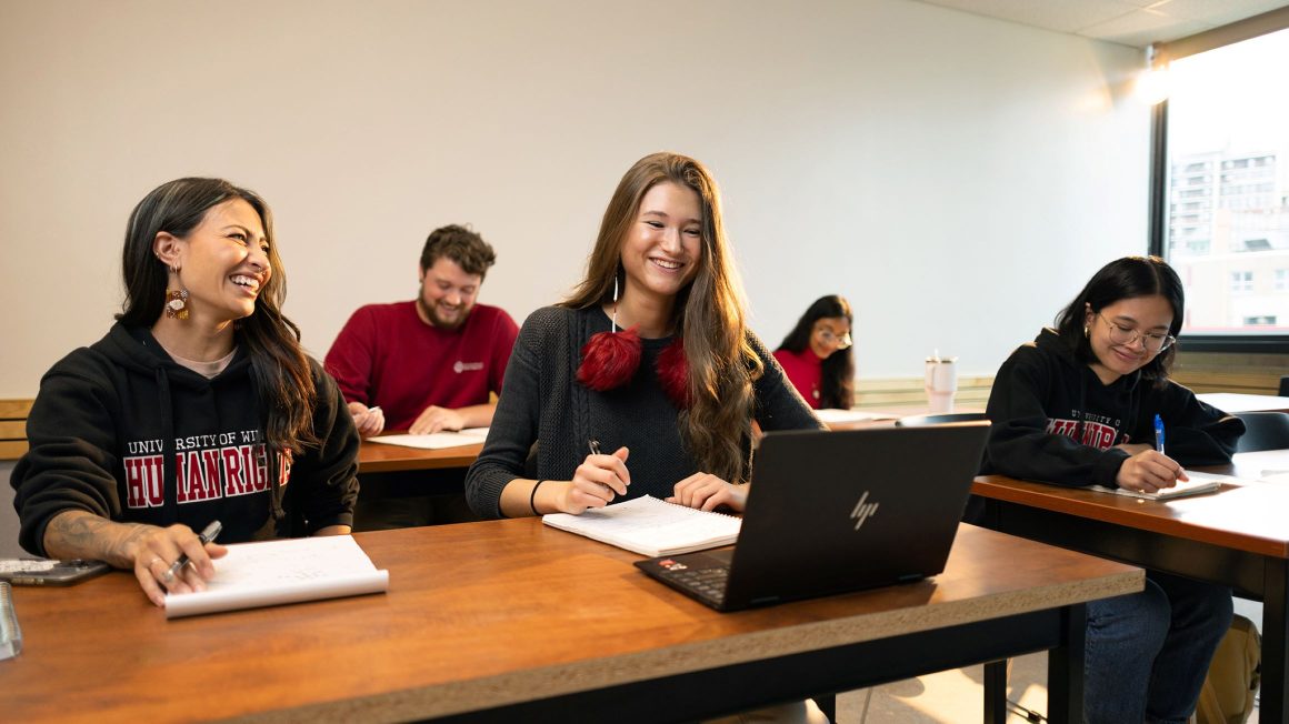 Students seated in a classroom with laptop and papers.