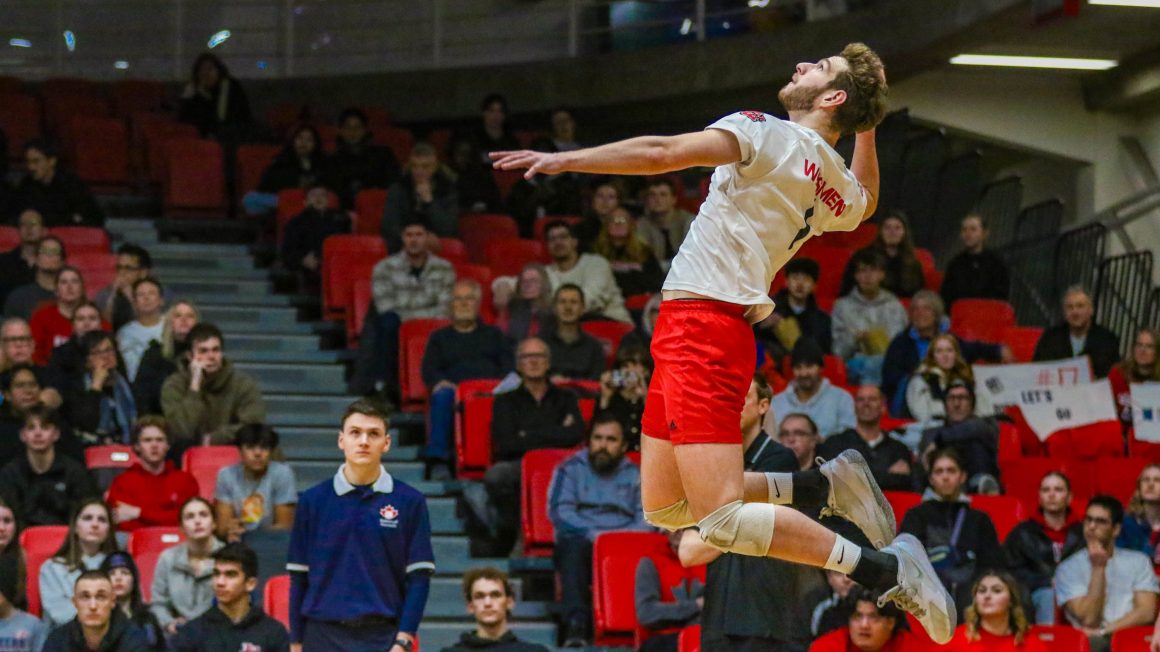 A male volleyball player jumps to hit a volleyball.