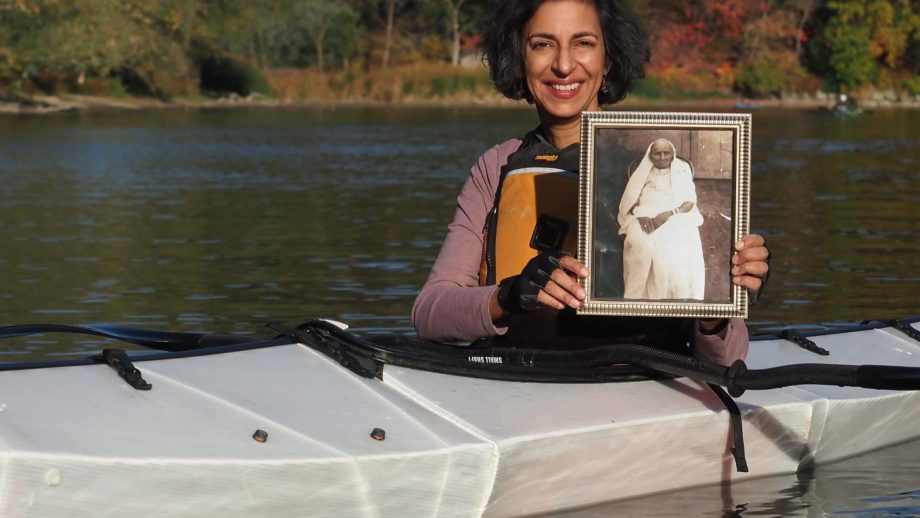 Heidi McKenzie holding a framed photograph of her great-great-grandmother Roonia, while seated in a boat.