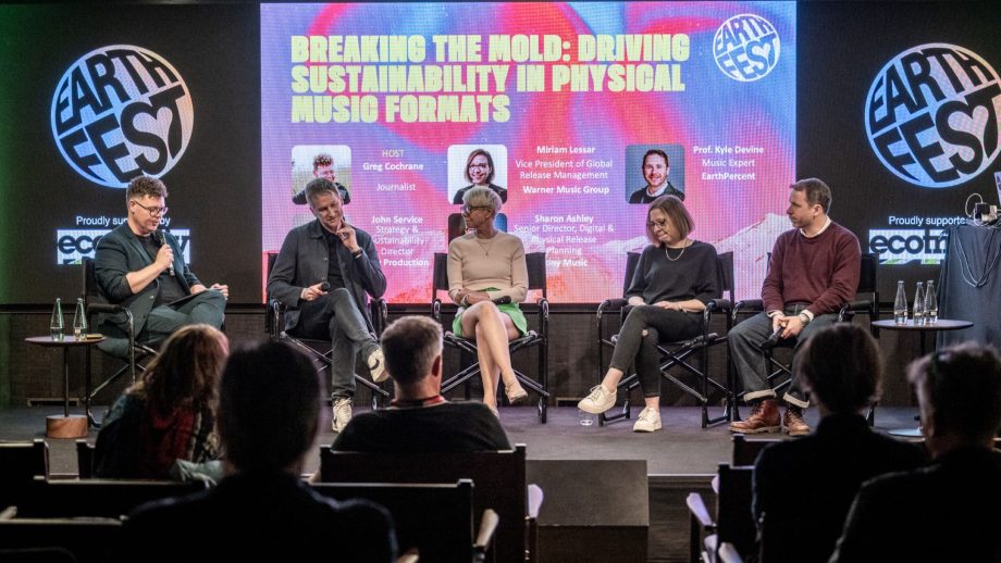 Five people sitting in chairs and holding microphones onstage during a panel discussion with a screen behind them.