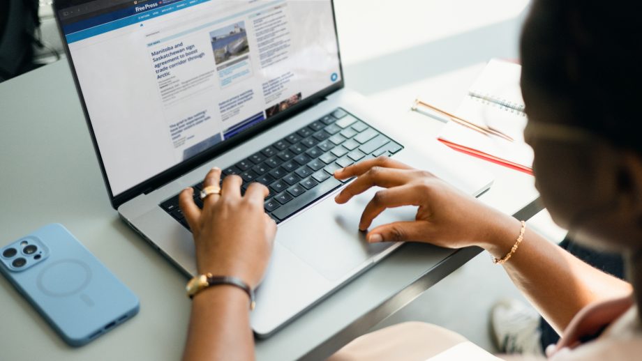 Hands hover over a laptop displaying the Winnipeg Free Press homepage.