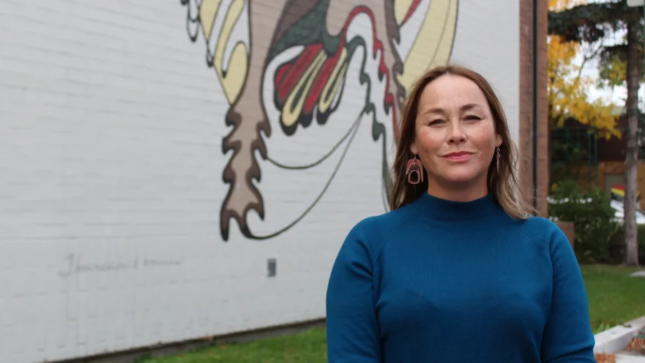 Jaimie Isaac standing in front of Daphne Odjig mural
