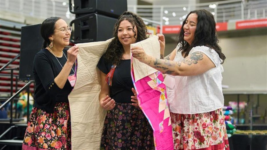 A student gets wrapped in a star blanket by two staff members.