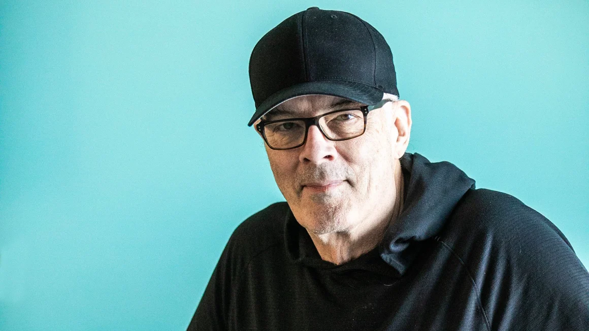 Scott Oake in a cap in front of a blue background.