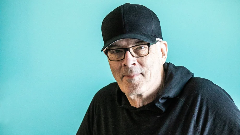 Scott Oake in a cap in front of a blue background.