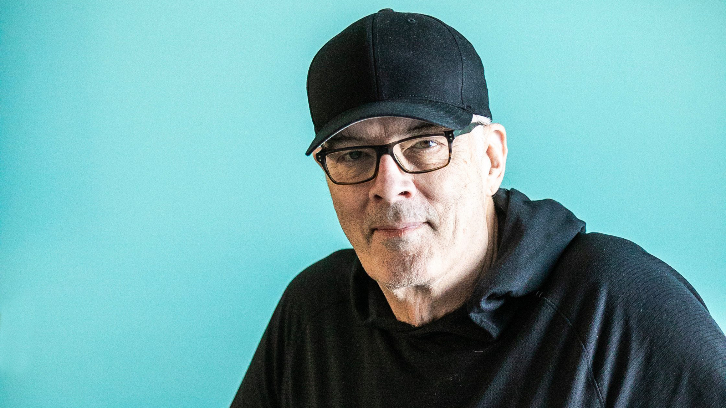 Scott Oake in a cap in front of a blue background.