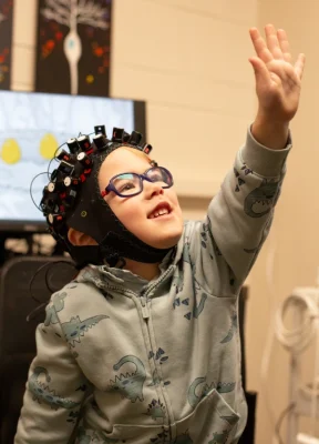 A young student wearing a device on his head reaches upwards