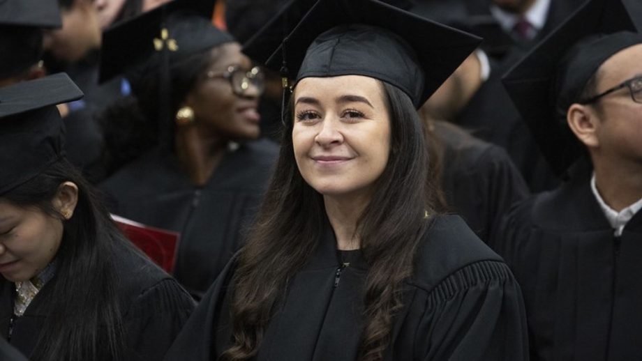 A graduate smiles at the camera in cap and gown.